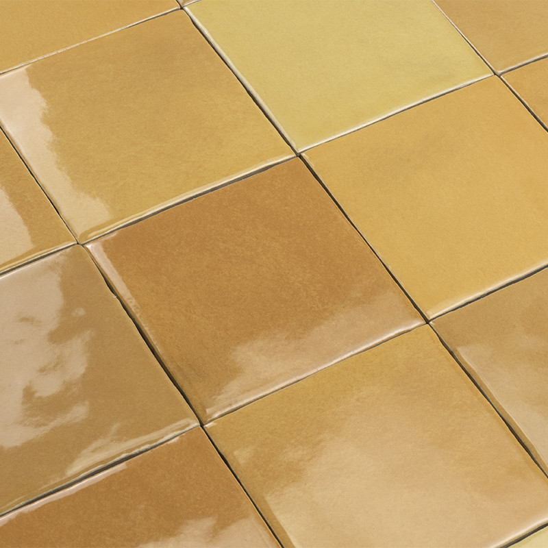 Carrelage en carreaux céramiques carrés beige et miel, surface vernissée brillante, joints fins et réguliers, disposition en quadrillage serré sur un plan horizontal.