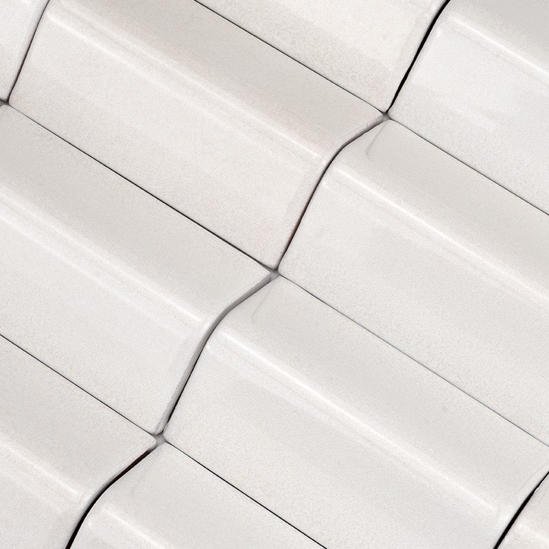 Carrelage céramique blanc à relief ondulé, carreaux rectangulaires assemblés en motif diagonal; joints fins sombres soulignent les arrondis et la finition brillante.